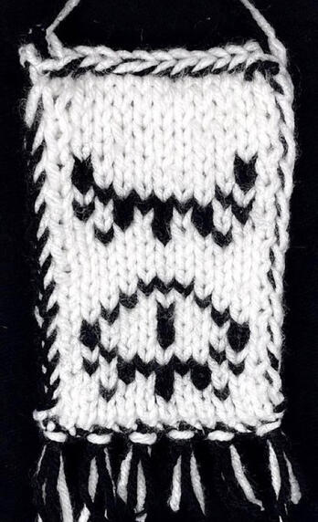 One side of a small, double-knit tapestry. Two eyes in black yarn, one above the other, on a white background. The eye at the top is closed, while the eye at the bottom is open.