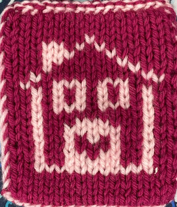 One side of a small, double-knit tapestry. The background is a dark pink; in light pink, there is a simplified image of a house with 2 windows and a rounded door. On the door is a heart, in the same dark pink as the background.